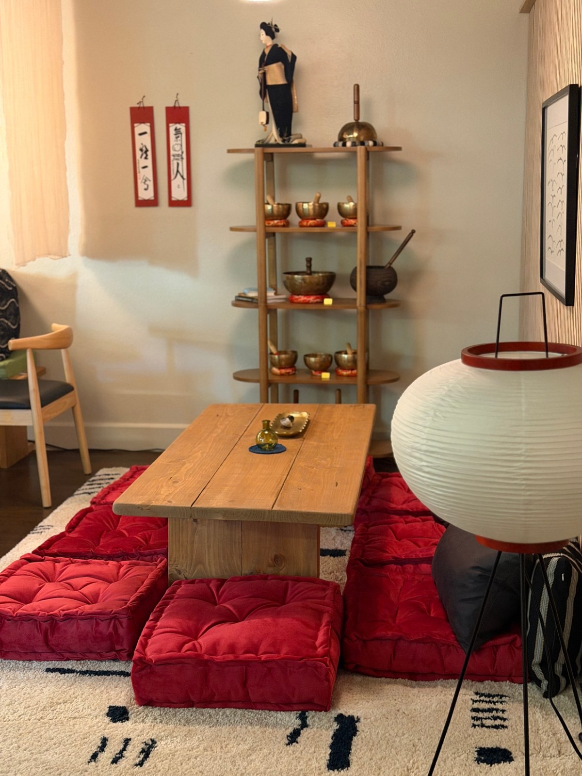 Low tea table with red floor cushions, singing bowls, and paper lantern